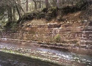Podmytý breh rieky Eyach s odkrytými horninami keuperu v meste Balingen (miestna časť Ostdorf), Nemecko
